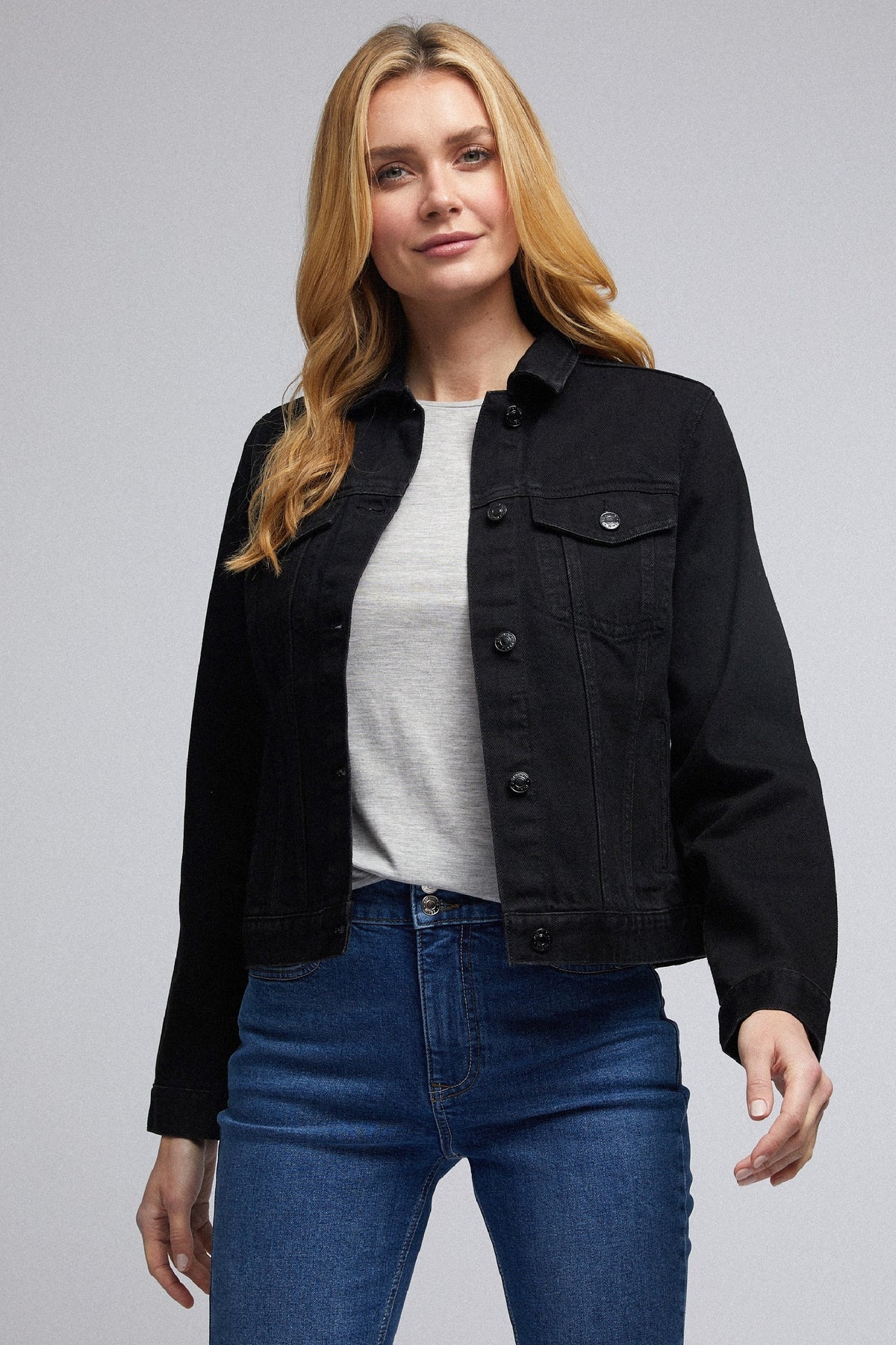 Stylish black denim jacket for women, featured on a model with wavy blonde hair, paired with a gray top and blue jeans.