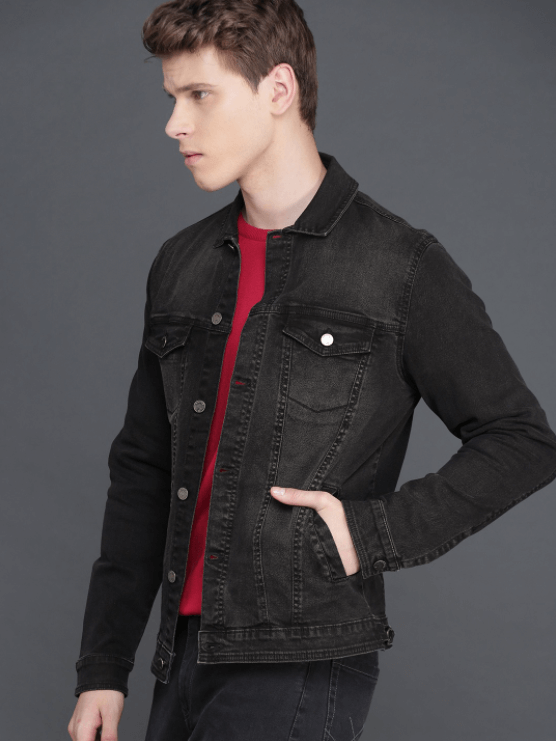 Stylish black denim jacket with model wearing red shirt and posing against gray background.