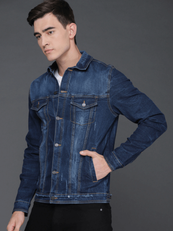 Man wearing a dark blue denim jacket with pockets and buttons, posing against a grey background.