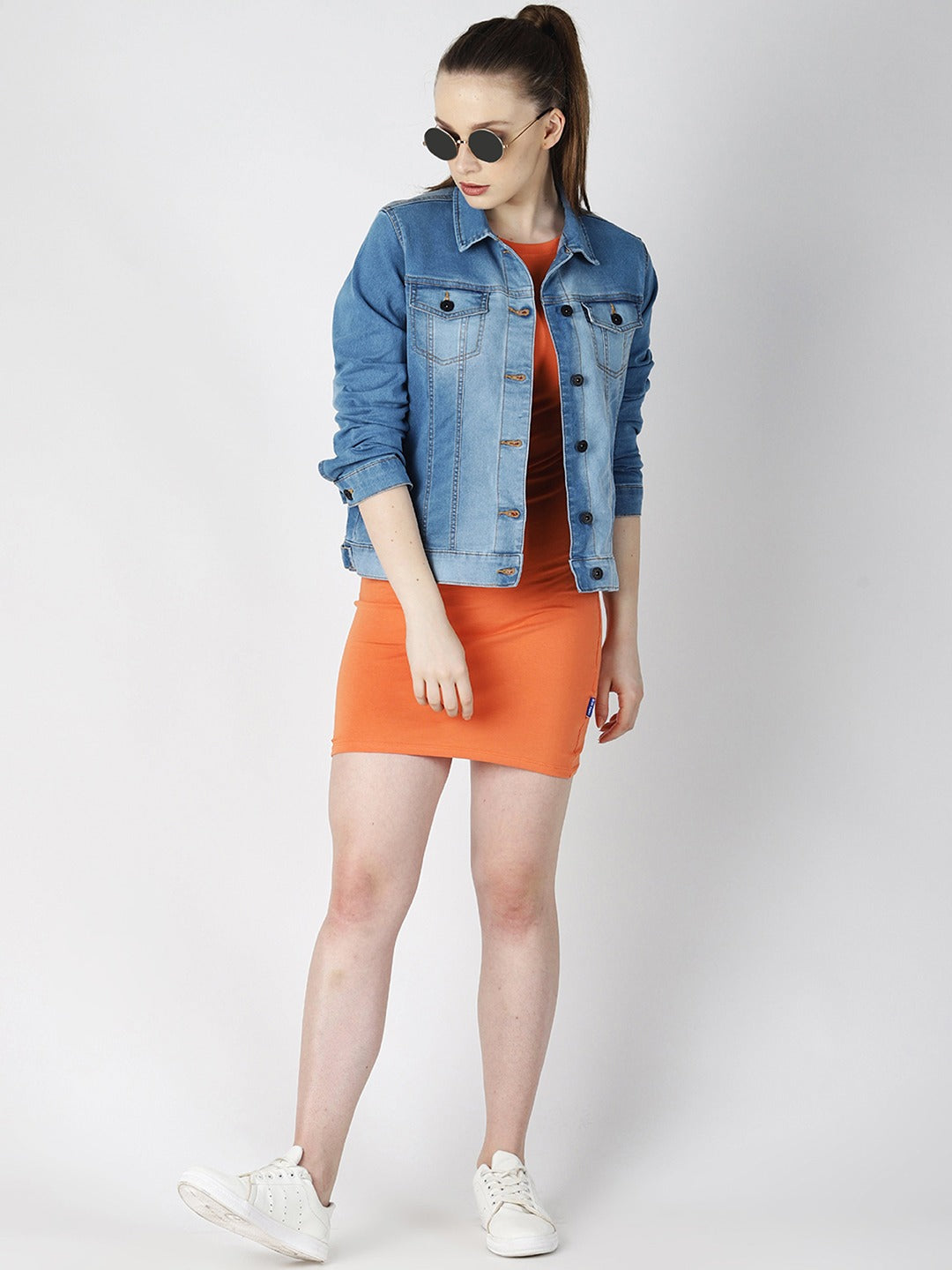 Stylish blue denim jacket, bright orange skirt, sunglasses, and casual white sneakers - a trendy, fashionable outfit showcased by the young woman in the image.
