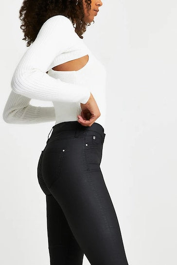Stylish black coated skinny jeans modeled by a woman with curly hair, showcasing a sleek and modern look.