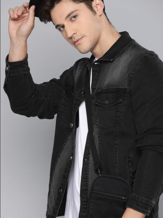 Black denim jacket worn by stylish young man against plain background.