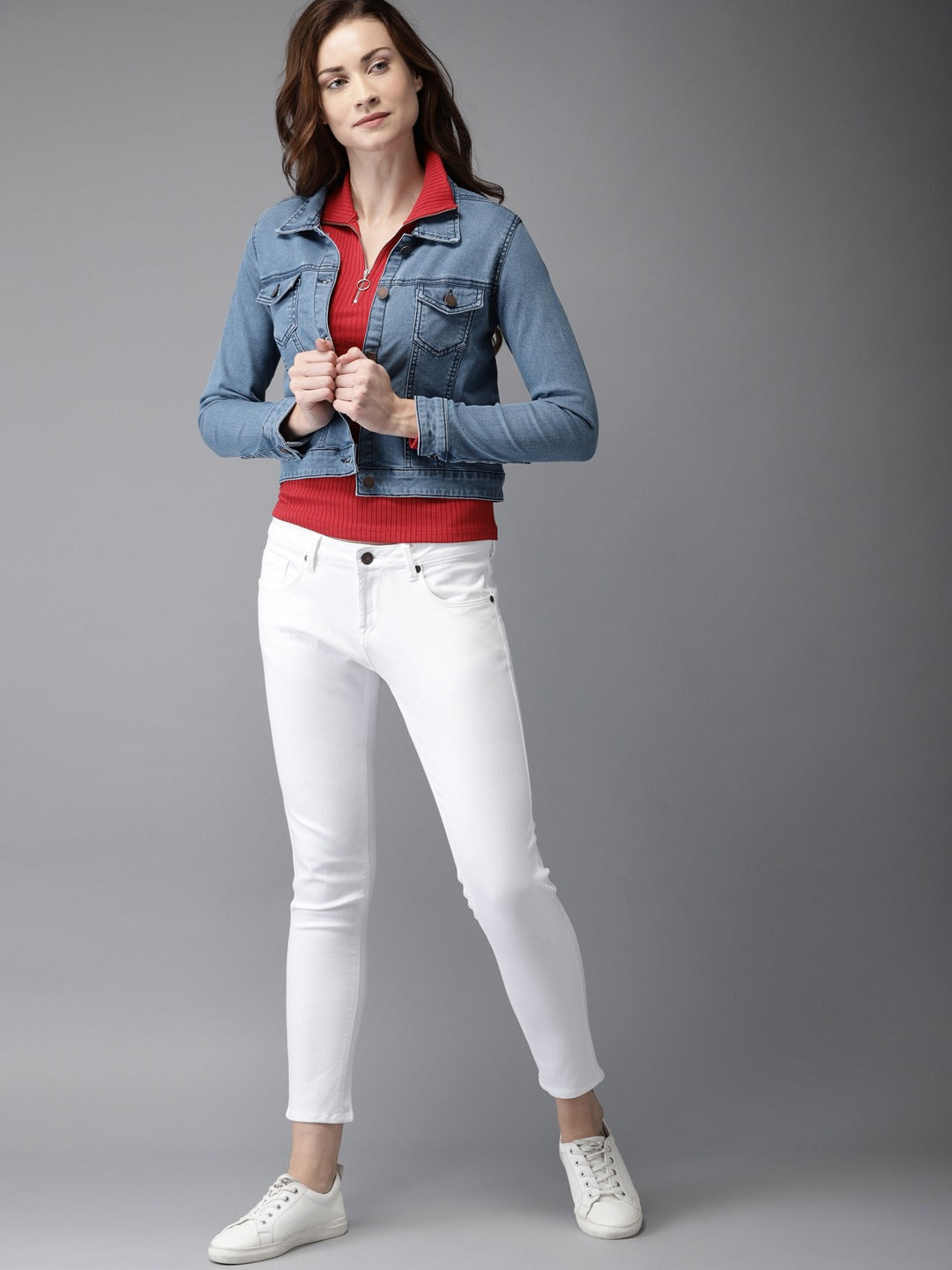 Stylish women's blue denim jacket, red crop top, and white jeans on model against grey background.