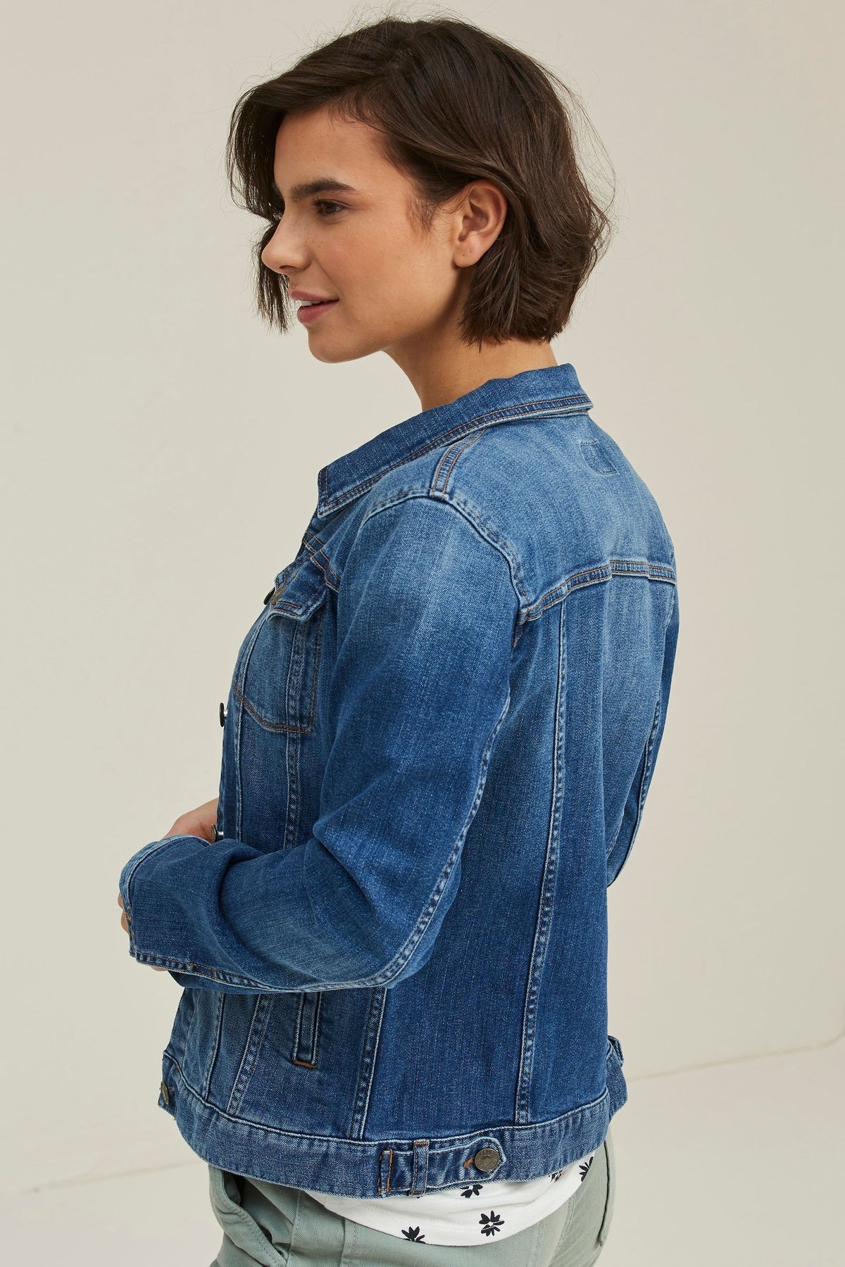 Blue denim jacket with ruffle detailing on the front, worn by a young woman with dark hair.