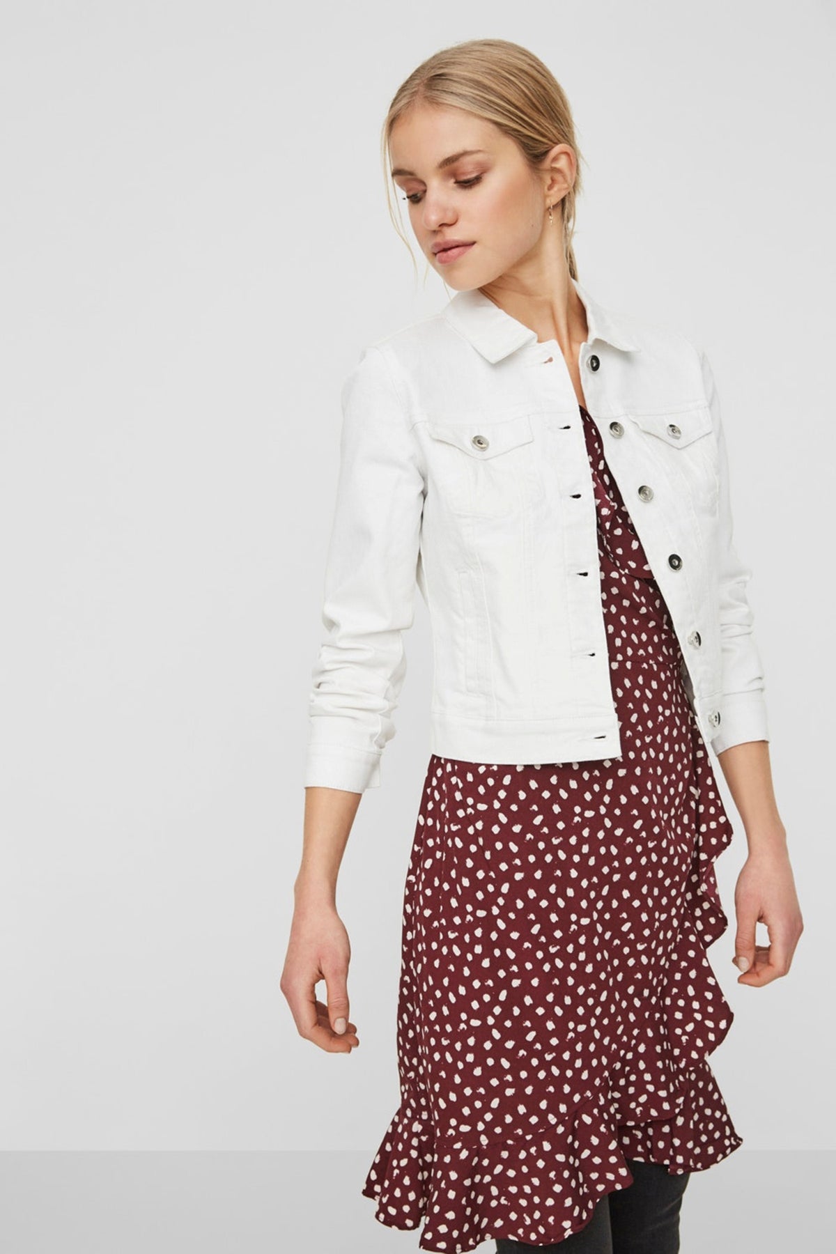 Fitted white denim jacket with button-up closure, worn over a burgundy polka dot dress, showcasing a stylish casual outfit.