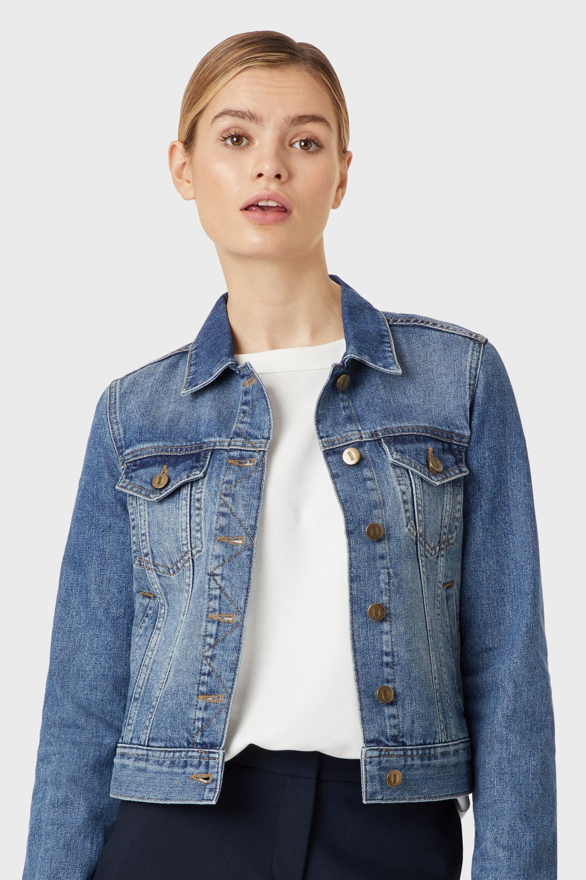 Classic blue denim jacket for women, featuring a clean, cropped silhouette and brass button detailing.