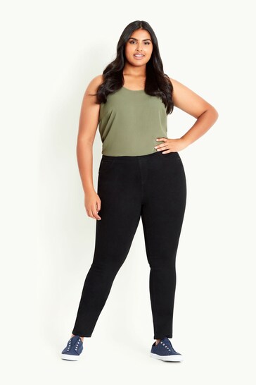 Plus-size woman wearing olive green tank top and black stretch leggings, standing against white background