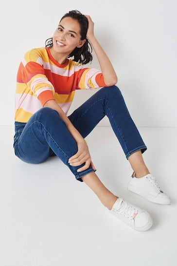 Colorful striped top, blue denim jeans, and white sneakers adorned by a smiling woman sitting on the floor.