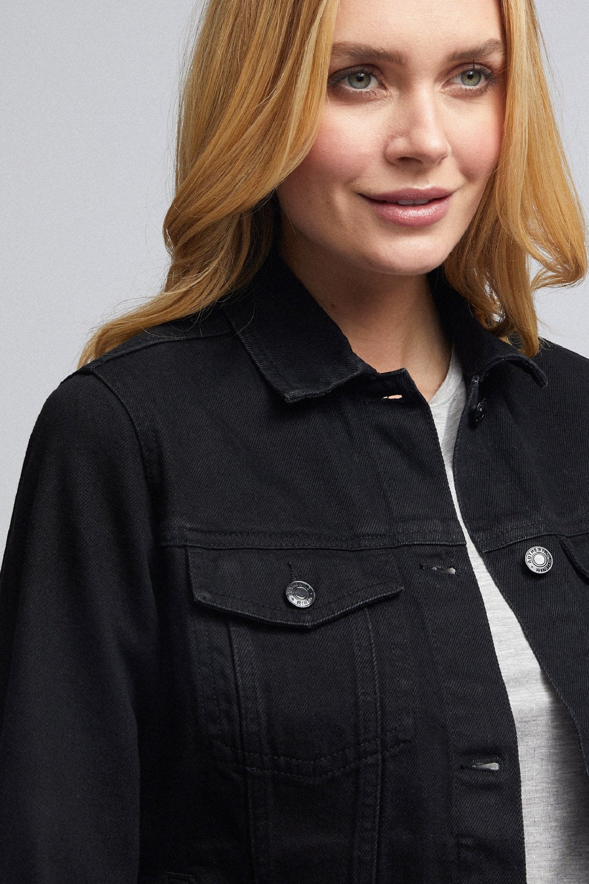 Stylish woman's black denim jacket with front pockets against plain background.