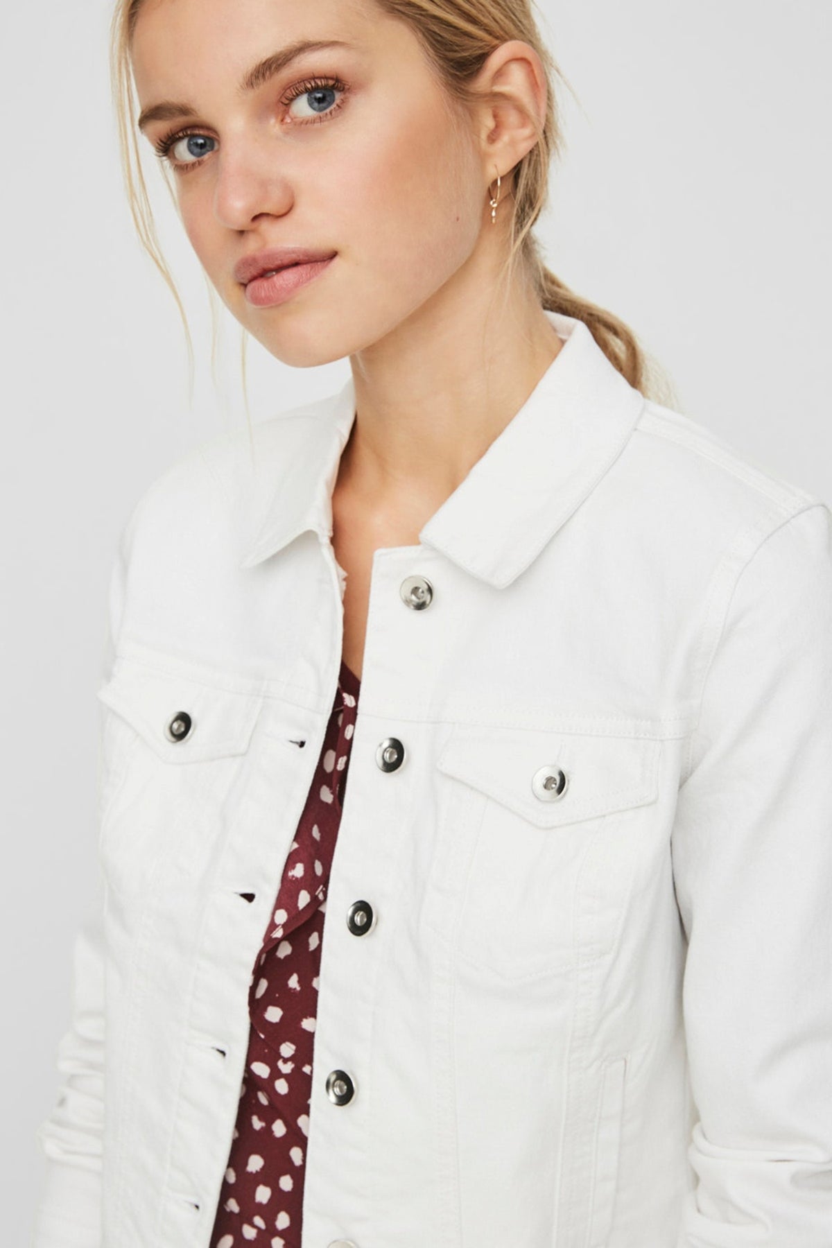 Fitted white denim jacket with button detailing, worn by a young woman with blonde hair against a plain background.
