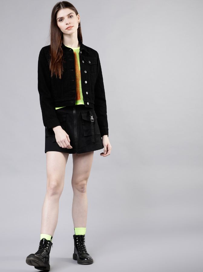 Black denim jacket for stylish young woman, neon green shirt and shorts, black lace-up boots, long brown hair.