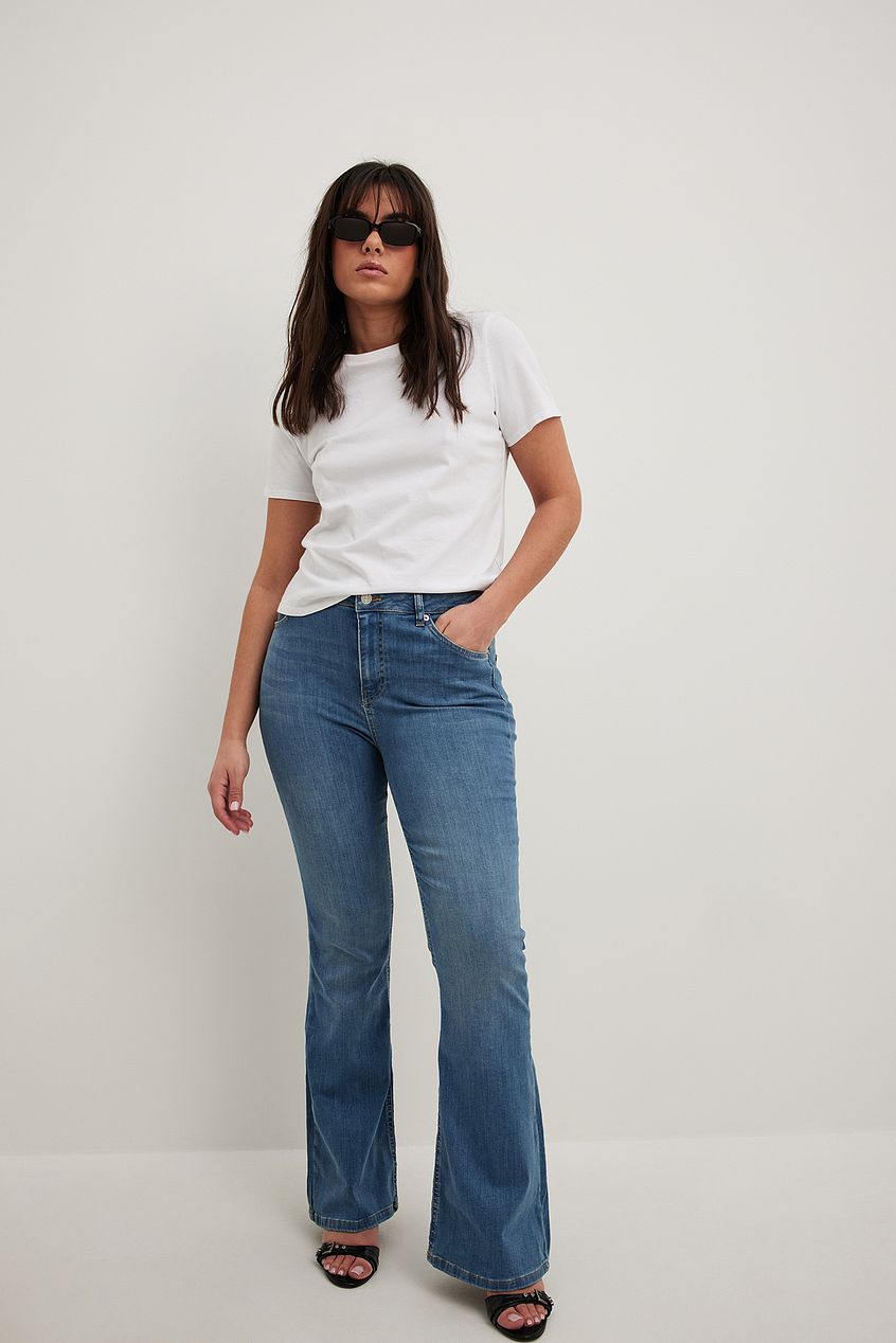 High-waist flared stretch denim jeans worn by a woman in a white top and sunglasses, posing against a plain background.