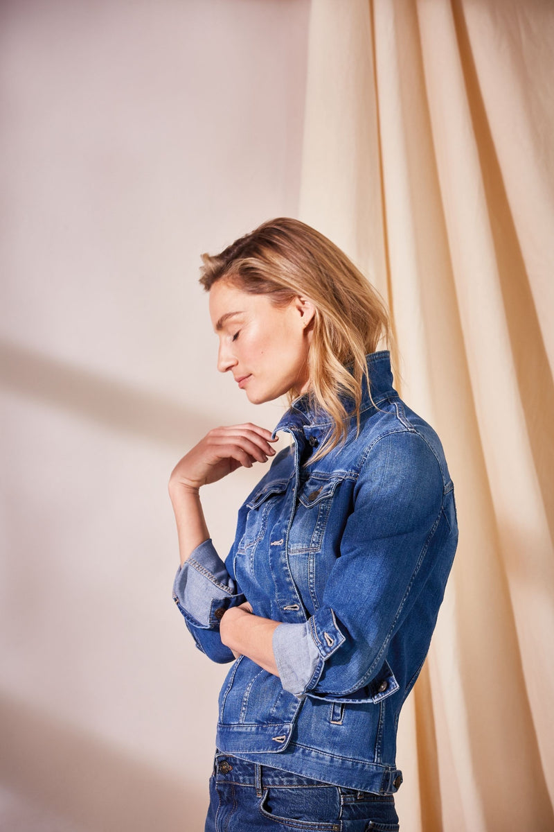 Stylish denim jacket worn by young woman with long blonde hair against peach background