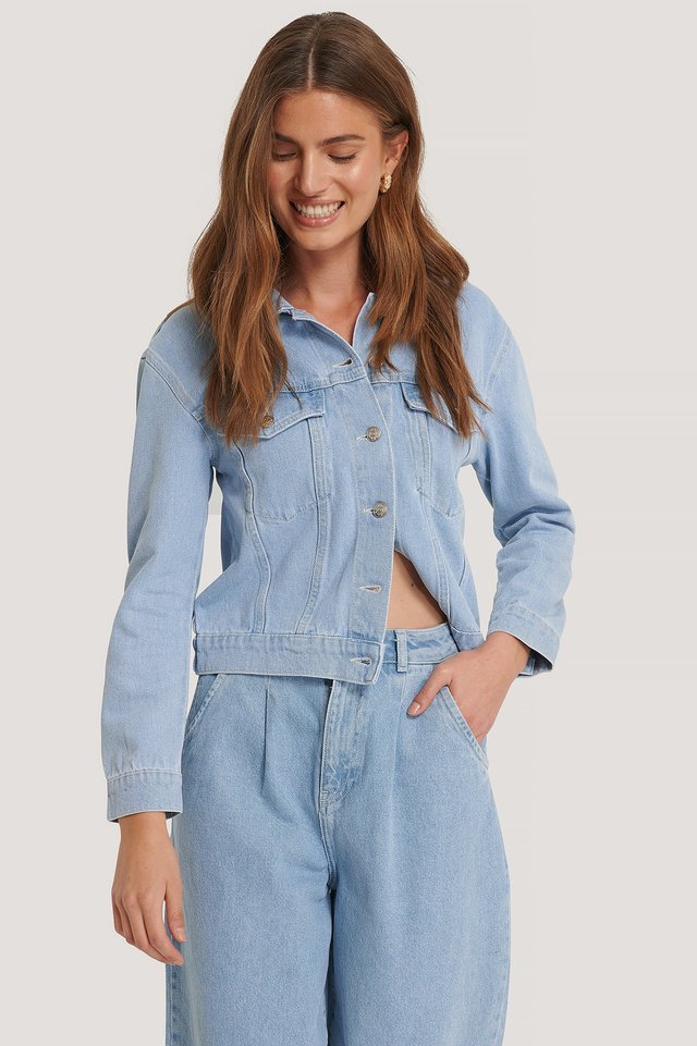 Women's light blue solid denim jacket with button closure, worn by a smiling young woman with long brown hair.