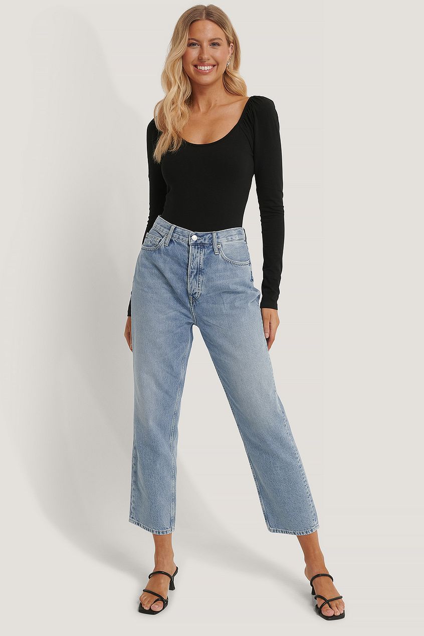High-waist denim jeans with relaxed fit, worn with a black long-sleeve body suit by a smiling blonde woman on a plain white background.
