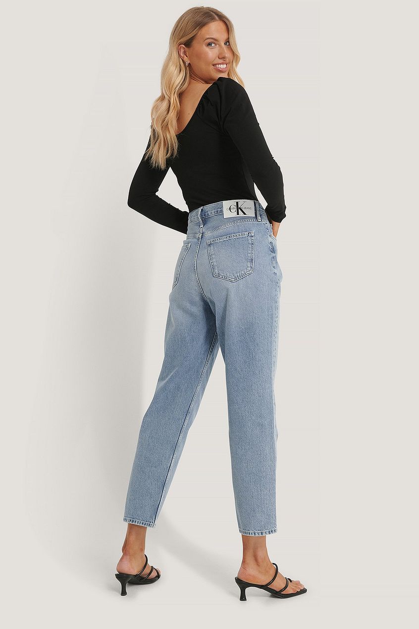 High-waisted light blue denim jeans from Ace Cart, featuring a classic straight leg silhouette and signature branding on the waistband. The model wears a black long-sleeved top, complementing the casual, comfortable aesthetic of the stylish denim bottoms.