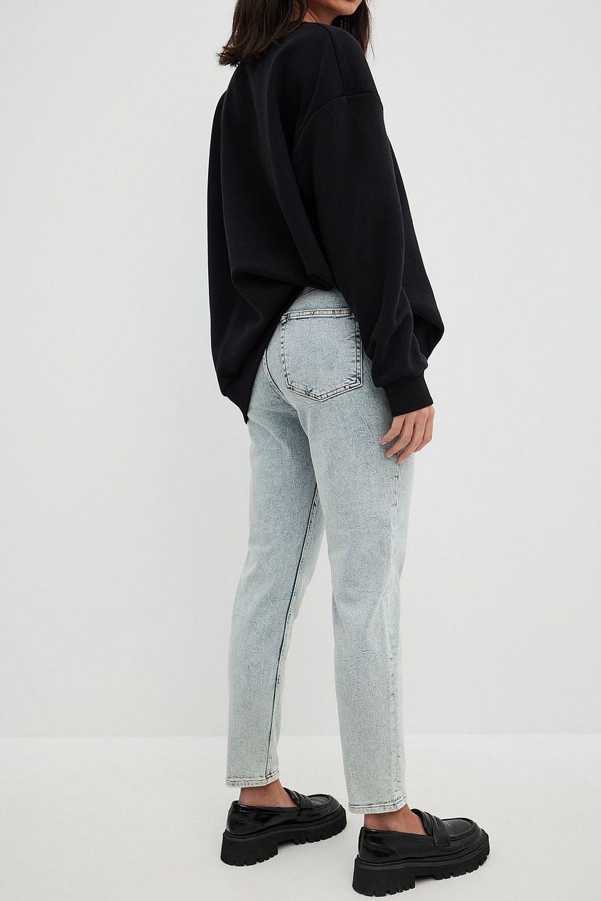 High-waist light-wash denim jeans with relaxed fit, styled with a black oversized sweater, and platform loafers in a minimalist setting.