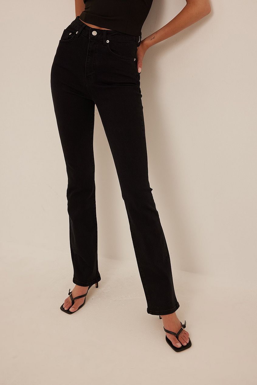High-waisted black denim jeans with a cut-out detail on the back, worn by a female model and paired with black strappy sandals.