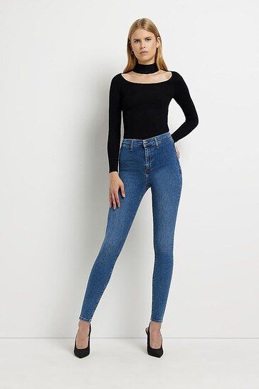 Stylish woman wearing blue skinny jeans and a black turtleneck sweater, showcased against a plain white background.