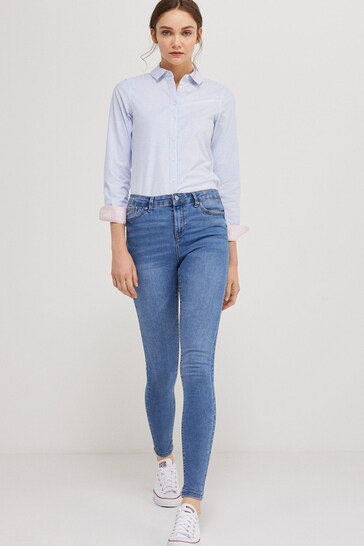 Blue wash skinny jeggings worn by young woman, paired with a collared white shirt and white sneakers