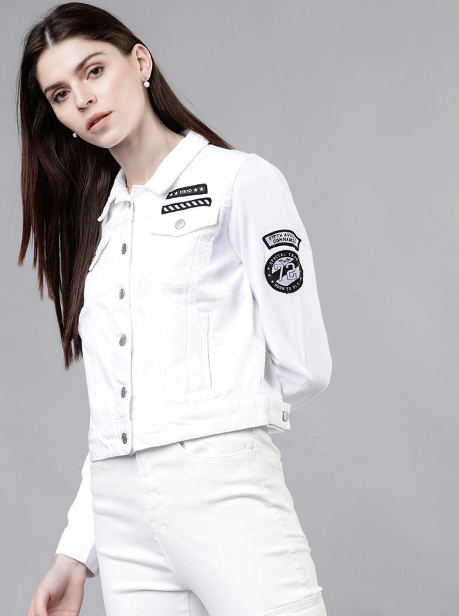 Stylish white denim jacket with fashion patches and logo details, worn by a young woman with long dark hair against a neutral background.