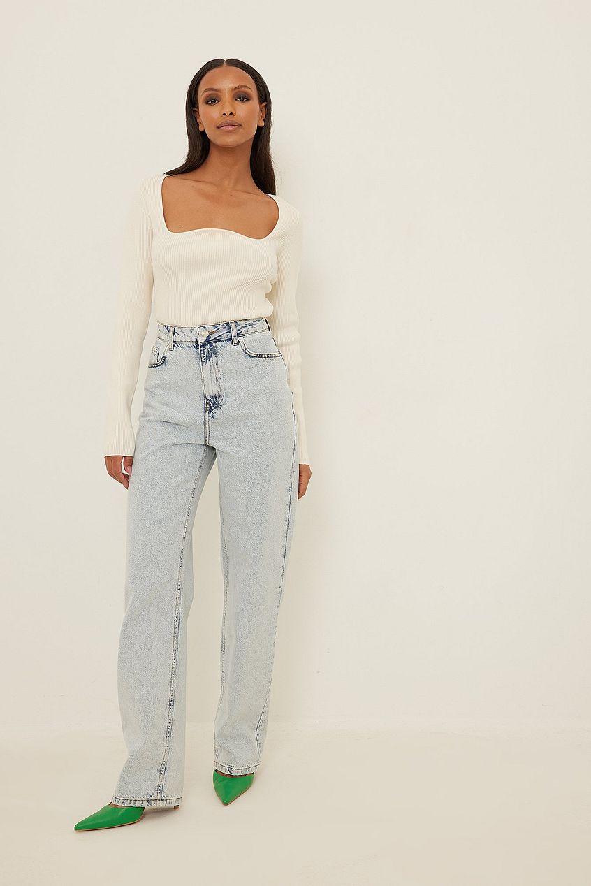 High-waist distressed denim jeans with asymmetric pockets, paired with a cozy off-white cropped sweater and vibrant green stilettos, showcasing a stylish and modern look.