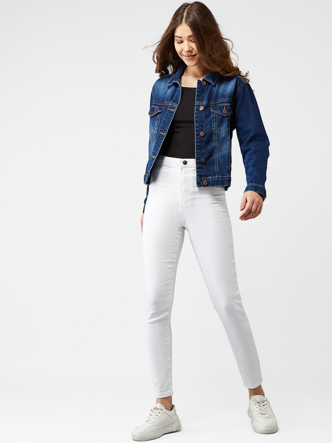 Stylish woman's blue denim jacket with white skinny jeans and casual sneakers.