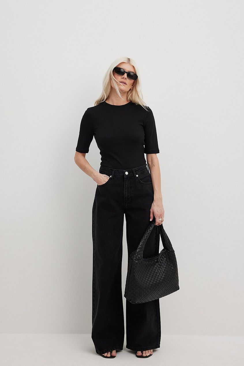 Organic Extra Wide Leg Denim - Stylish woman in black top and pants holding a leather tote bag