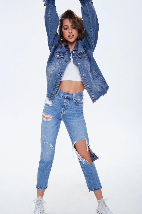 Fashionable cropped denim jacket with distressed details, worn by a young woman against a white background.