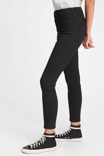 High-waisted black jeggings with ripped knees, worn with black and white sneakers on a white background.