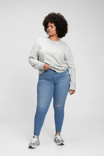 High-waisted ripped knee universal jeggings on a curvy female model with a casual grey sweater and sneakers.
