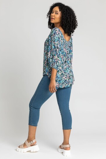 Colorful floral patterned cropped jeggings worn by a young woman with curly dark hair, showcased in a full-length portrait against a plain background.