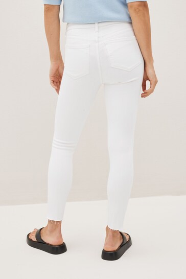 High-waisted white jeggings with ripped knees, displayed on a female model against a white background.
