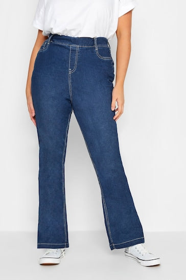 Dark blue plus-size curvy bootcut jeggings with stitched details, worn by a person standing against a plain background.