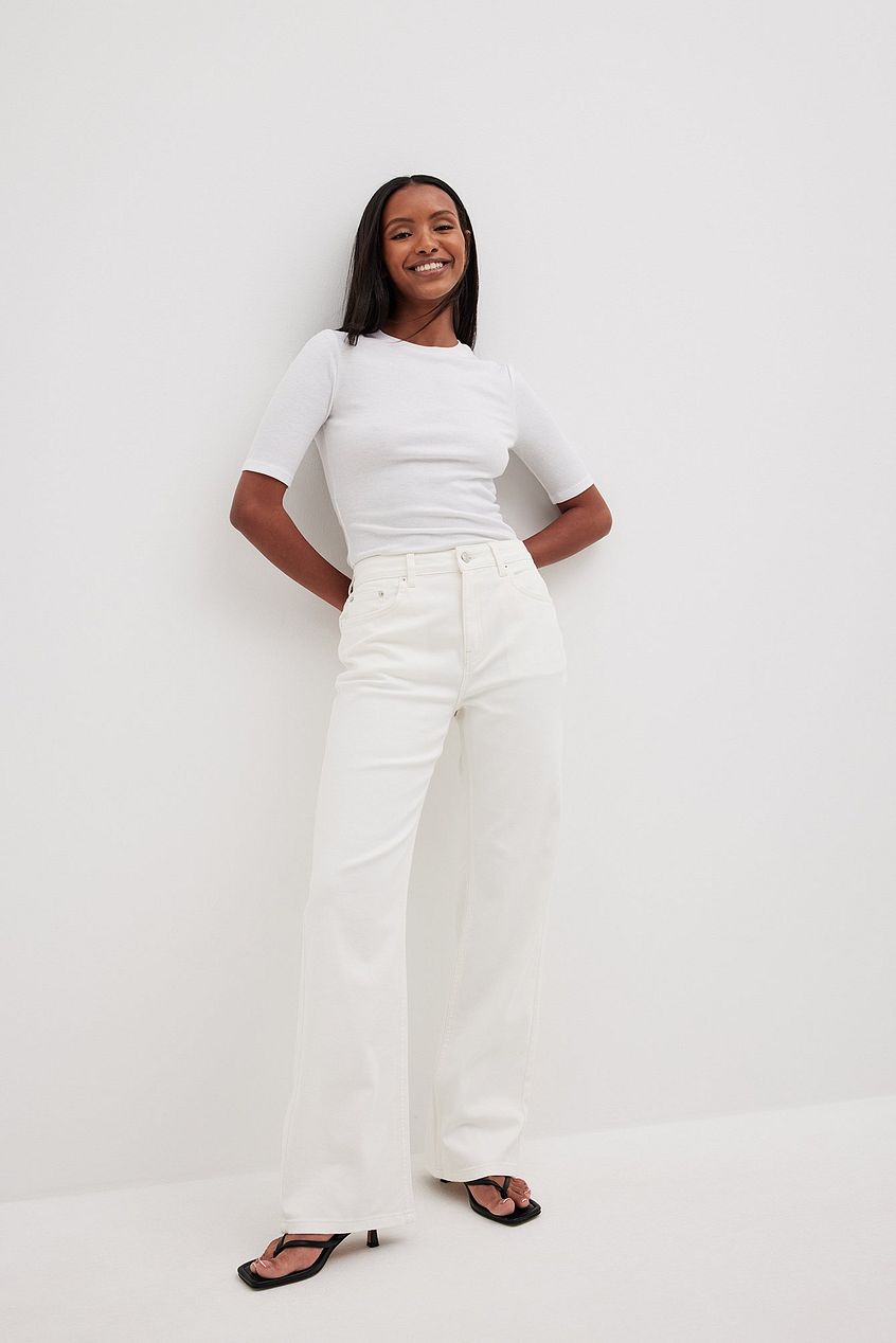 Stylish woman in white top and jeans posing against white background