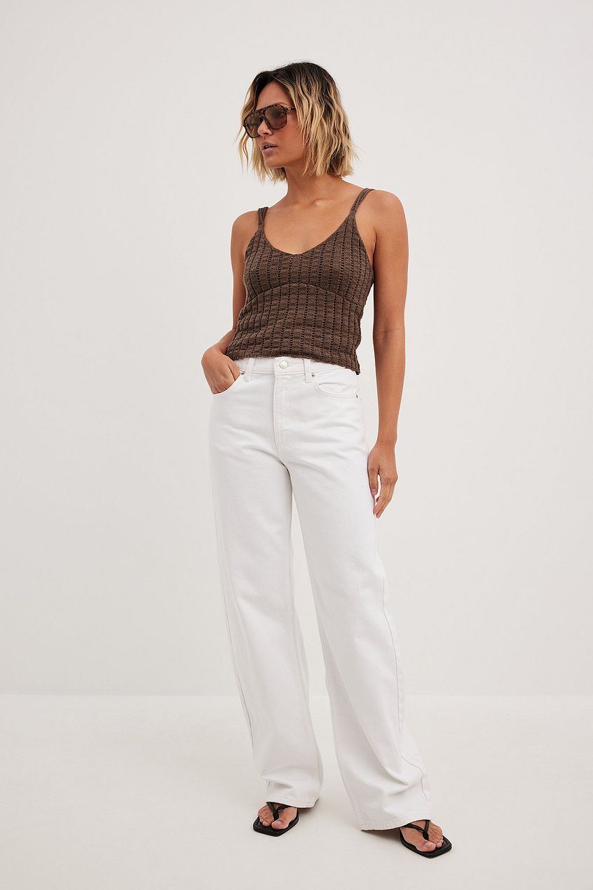 Loose mid-waist white jeans, ribbed brown tank top, and sunglasses worn by woman in product image.