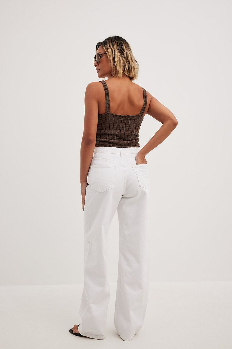Brown ribbed crop top and white high-waisted wide leg jeans worn by a woman against a plain white background.