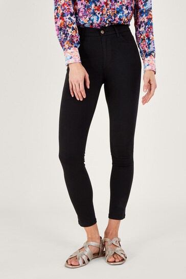 Slim-fit black skinny jeans with a high-waisted design, worn by a female model in a floral print blouse against a white background.