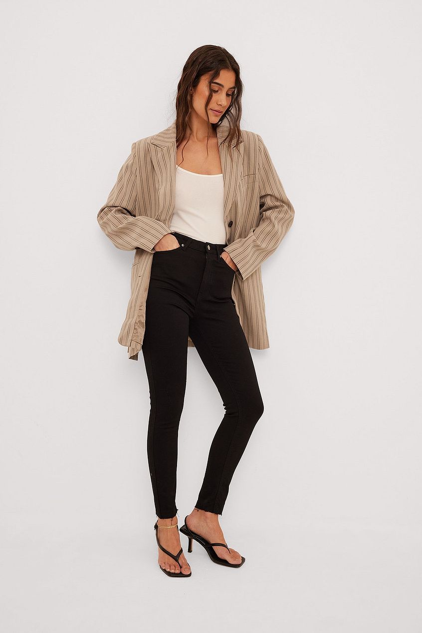 Skinny High Waist Raw Hem Jeans - Casual chic outfit featuring figure-flattering black denim jeans, a fitted white tank top, and a beige striped lightweight jacket from the Ace Cart clothing brand.