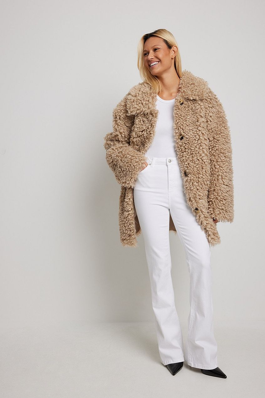 Flared High Waist Stretch Jeans modeled in a white background, featuring a woman wearing a beige fuzzy coat and smiling.
