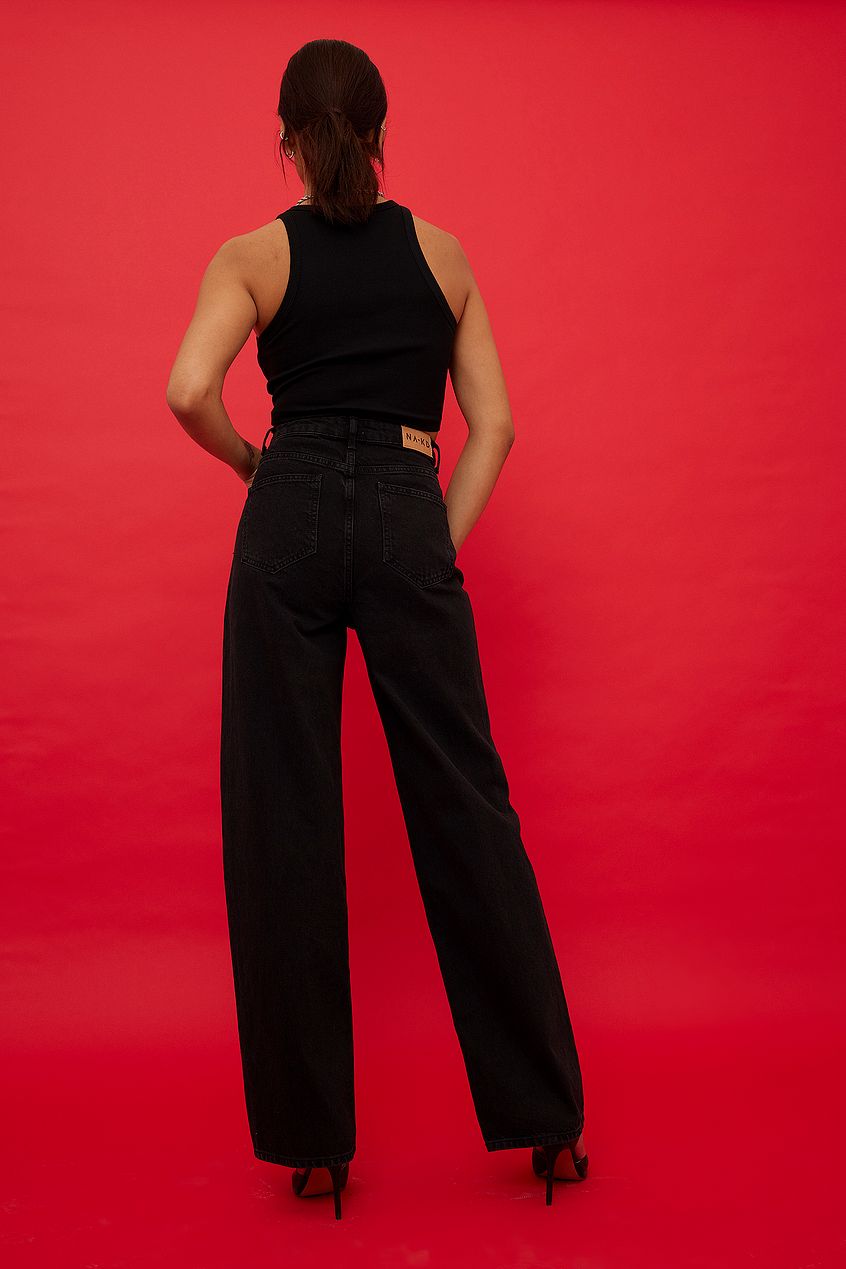 Stylish black jumpsuit with wide legs, sleeveless design, and a high waistline, set against a vibrant red background.