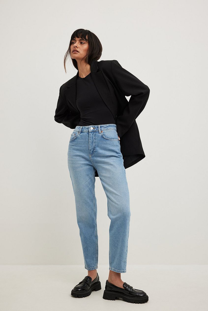 High-waist blue denim jeans with a black cropped jacket showcased on a female model against a plain white background.