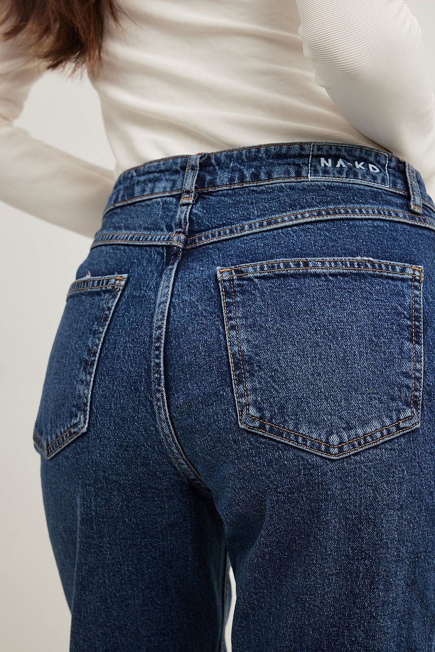 High-waist dark blue denim jeans with back pockets, featured on a partial view of a person's body.