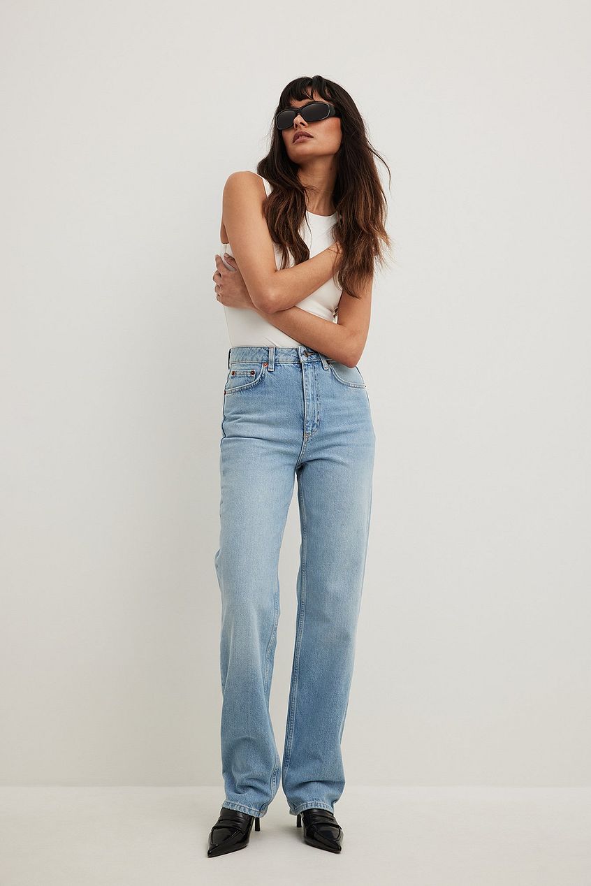 High-waist straight leg denim jeans in light blue, worn by a stylish woman with sunglasses and a sleeveless top against a plain white background.
