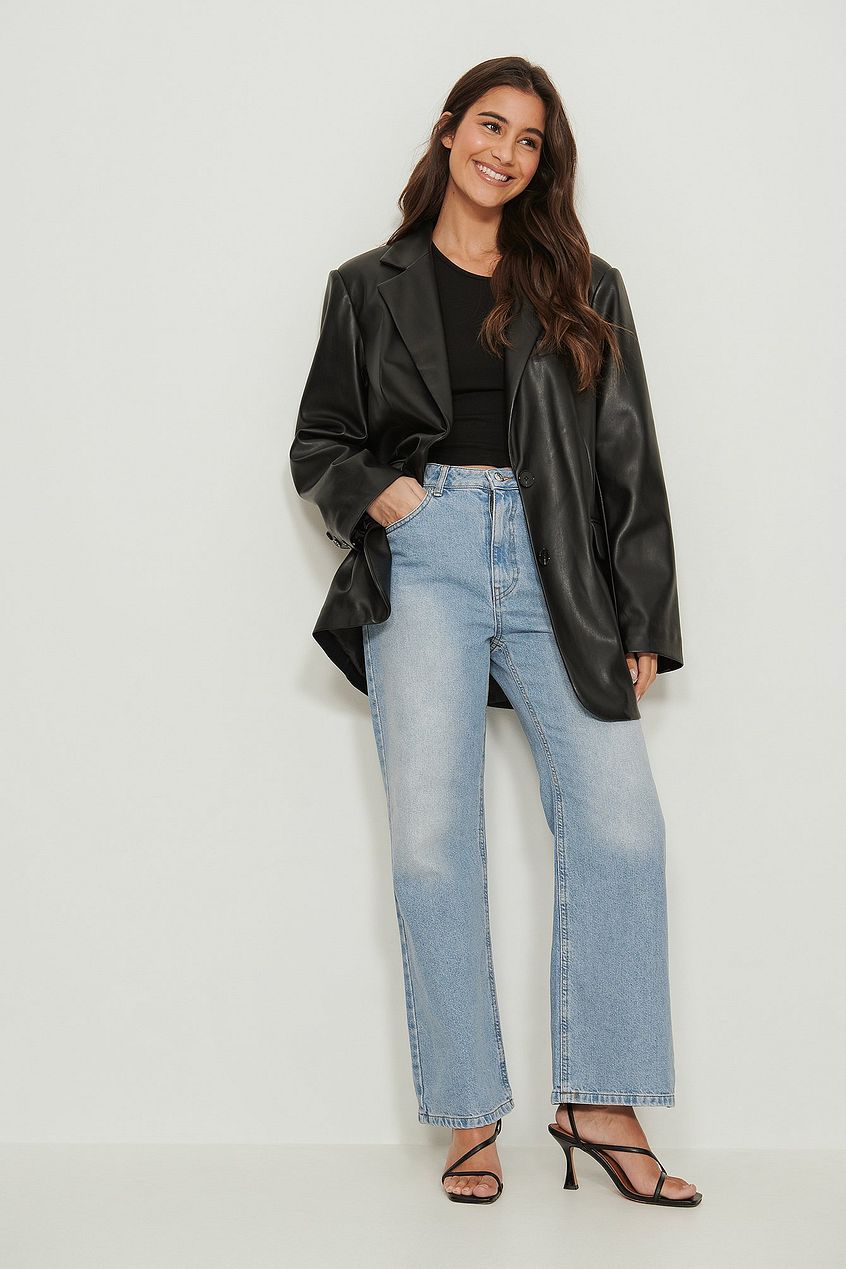 Stylish woman in high-waisted relaxed-fit denim jeans, black leather jacket, and heels poses confidently in front of a plain white background.