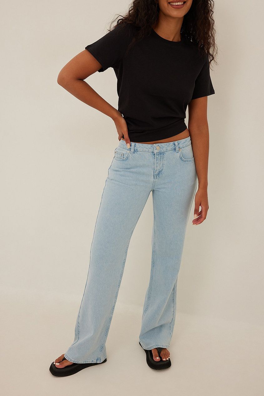 Stylish low waist light blue denim jeans with a relaxed fit and a young woman wearing a black t-shirt, showcasing the product on a plain background.