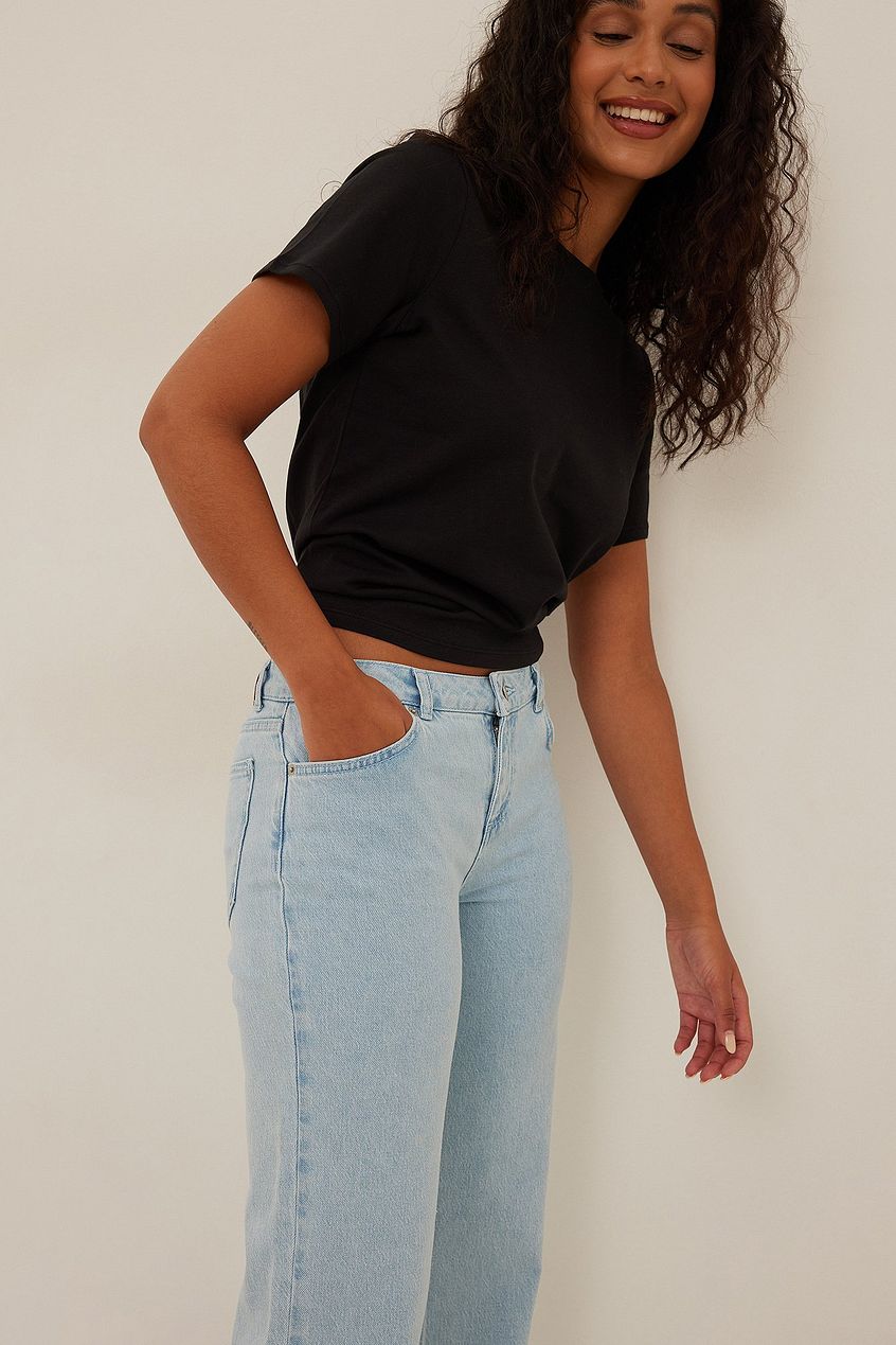 Stylish woman in black top and light-wash denim jeans from Ace Cart, smiling with confidence.