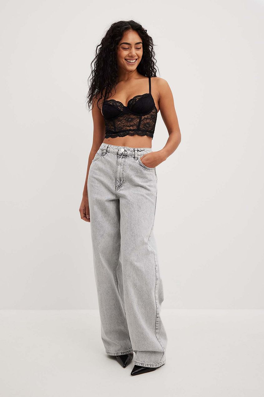Loose low waist long gray jeans worn by a woman with curly dark hair in a black lace crop top.