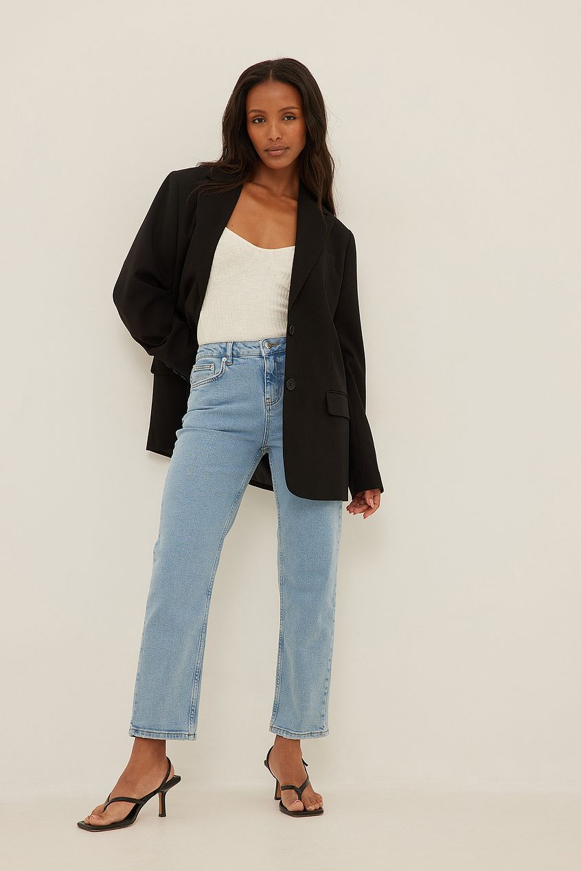 Mid Waist Slim Leg Light Wash Denim Jeans - Stylish woman modeling fashionable denim jeans and black blazer against neutral background.