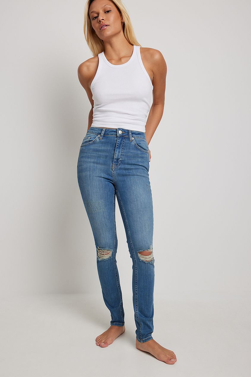 Skinny high-waist destroyed denim jeans with a white tank top, showcasing a stylish and casual women's fashion look.
